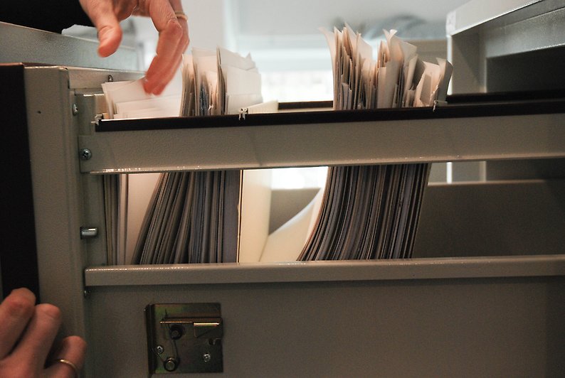 Registrator bläddrar bland akter i hängmappar i ett utdraget arkivskåp.
