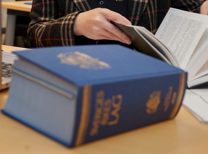 lagbok i förgrunden och händer som bläddrar i bok i bakgrunden